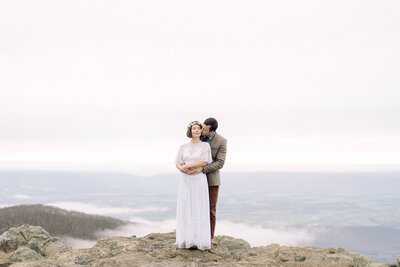 Bride and groom standing hand in hand with a mountain lake behind them during their intimate Virginia elopement, photographed in natural light and soft tones.

