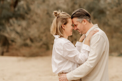 Verliefde papa en mama met hoofden tegen elkaar aan terwijl ze glimlachen naar elkaar en elkaar vasthouden bij de duinen van Herperduin