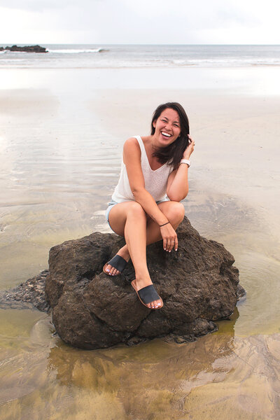 Lifestyle photographer, Samantha Okazaki, poses on a rock at a beach