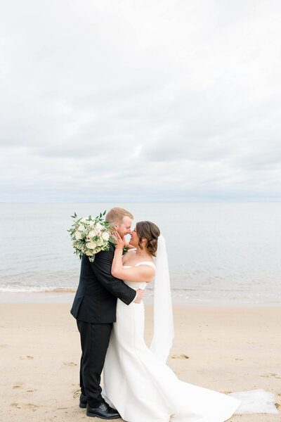 Bride groom belly button to belly button while going nose to nose. behind the ocean.