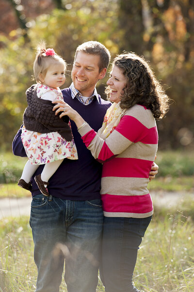 Two parent's smiling at their child as one holds them on their hip 