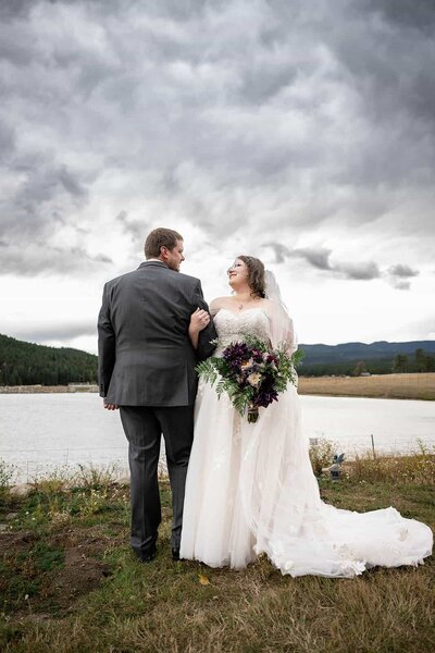 Bride holding grooms arm next to a lake on a stormy day