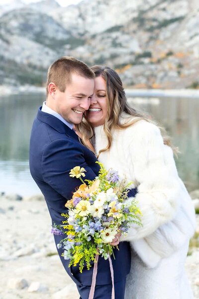 A bride and groom laugh together in front of a beautiful mountain view on their mammoth lakes wedding day. 