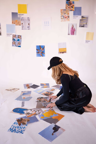 ALT: Grace kneeling on floor looking at scattered client project papers on floor and taped to wall in front of her