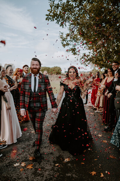 Alternative wedding couple walk through as their guests throw confetti. 
