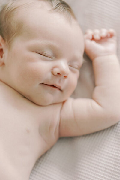 Close up of a newborn baby sleeping with his arms raised.