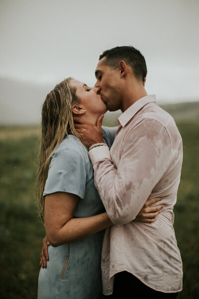 A man holds his fiance's neck as he kisses her in the rain