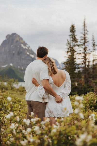 Couple leaning on each other facing away in a Montana meadow of white flowers, looking at the distant mountains.