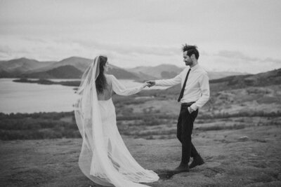 Bride and groom holding hands during a romantic elopement in the Scottish Highlands, with sweeping views of the mountains and lochs behind them.