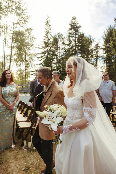 An emotional bride walks down the aisle to her groom, accompanied by her father, 