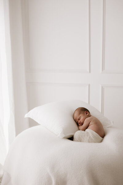  Newborn baby peacefully sleeping on a white bed in a Sydney photography studio, wrapped in soft textures with natural window light.