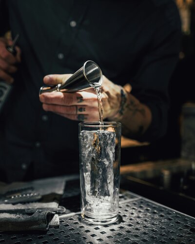 Bartender pouring shot into cocktail glass