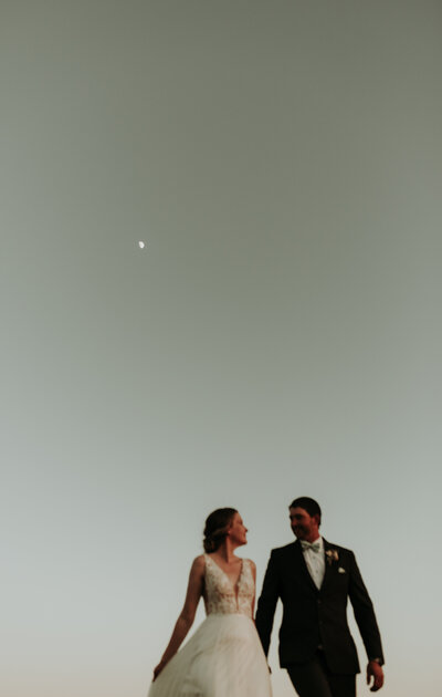Bride and Groom facing each other with the moon behind them and a beautiful blue sky. Arthur Ontario - Wedding Photography