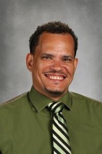 A male principal in a green shirt and tie smiles confidently, endorsing Gamably 