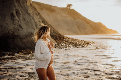 A woman posing for her maternity portraits at a Christchurch beach while being photographed by Christchurch photographer Lucy Jane Photography