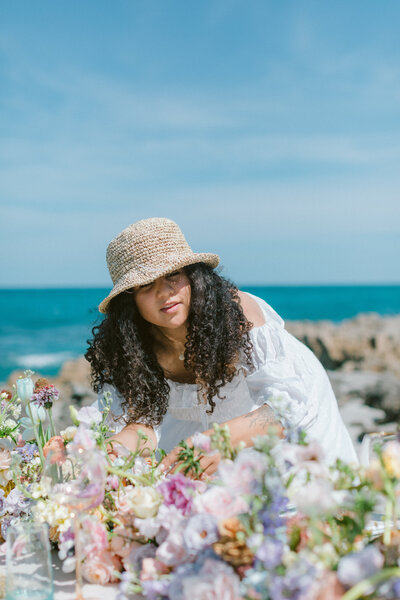 Natalia working on a beach lush floral tablescape with bright blue beach water in the background.