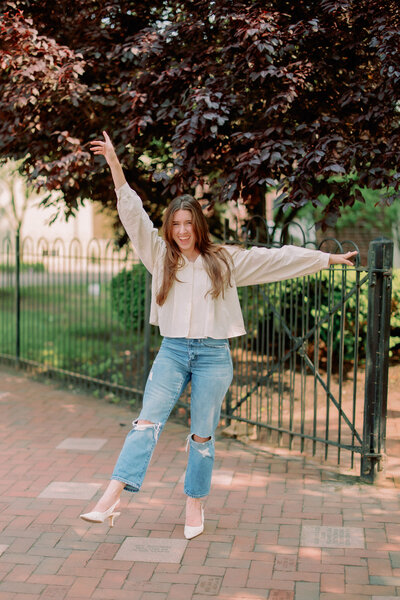 A person poses with their arms out in front of a tree.