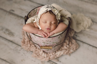 A newborn baby girl posed in a bucket prop with a bonnet in Charleston, South Carolina