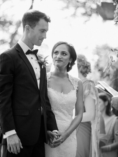 Black and white photo of bride and groom holding hands and looking at each other