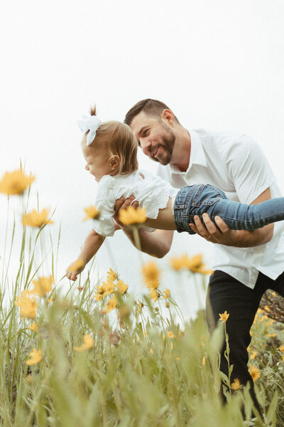Father playing with his daughter in a field of yellow wildflowers.