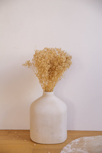Dried baby's breath in a stone vase sitting on the ground.
