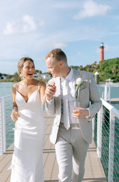 newly married walking on a dock towards the camera with the jupiter lighthouse in background