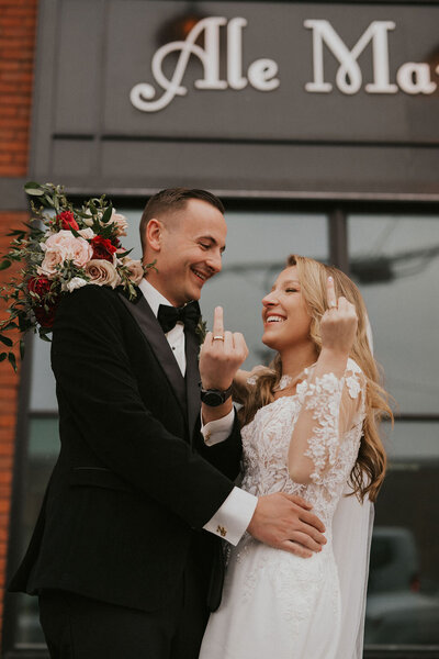 Fun-loving couple showing off their wedding rings outdoors by flipping their ring fingers at the camera during their New York City wedding, captured by Dom Augustine.