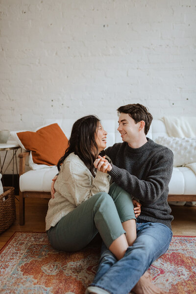 couple sitting on living room floor, holding hands and laughing