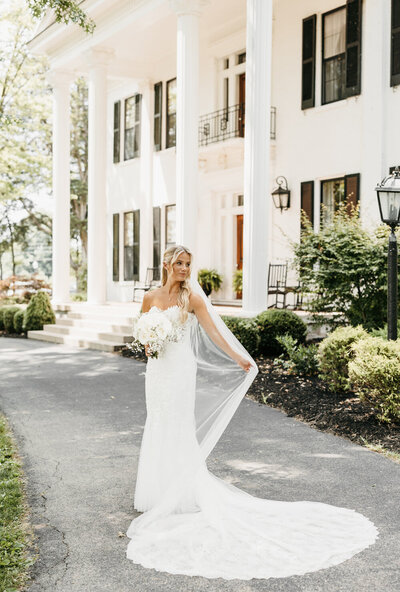 Bride in a fitted lace gown holding her veil in front of Ashford Acres Farm.