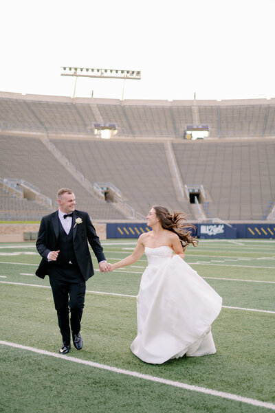bride and groom holding hands while walking on a football field