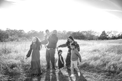 black and white photo of a family walking outdoors. The sun is shining bright in the background and they are walking and smiling.