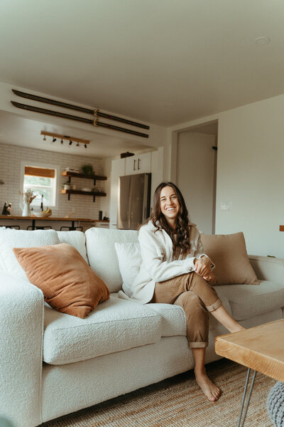 Woman with brown hair and a tan sweater seasoning food in the kitchen