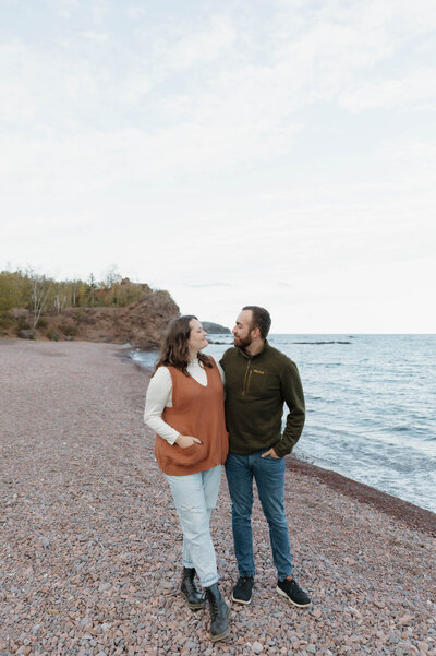 A couple looking at each other and walking along the water 