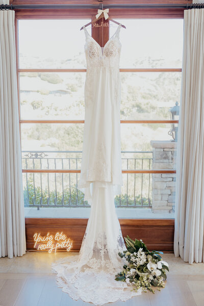 wedding dress hanging in a window with a neon sign