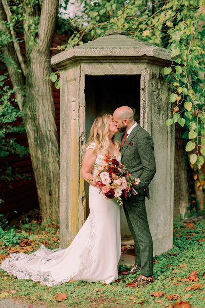 Newlyweds kiss in front of a small stone awning at Prallsville Mills.