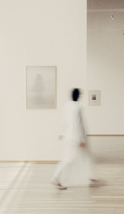 white room with a woman in a white outfit with dark hair walking away from the photographer facing away from shot