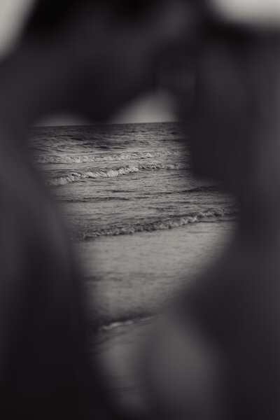 Black and white photos with two people resting their heads together and the camera is focused through their chest on the ocean