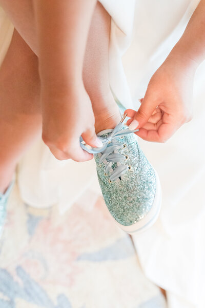 A light and airy photo of a bride tying her blue glittery shoes before her wedding at the Tate House in Georgia by Jennifer Marie Studios, Atlanta's best wedding photographer.