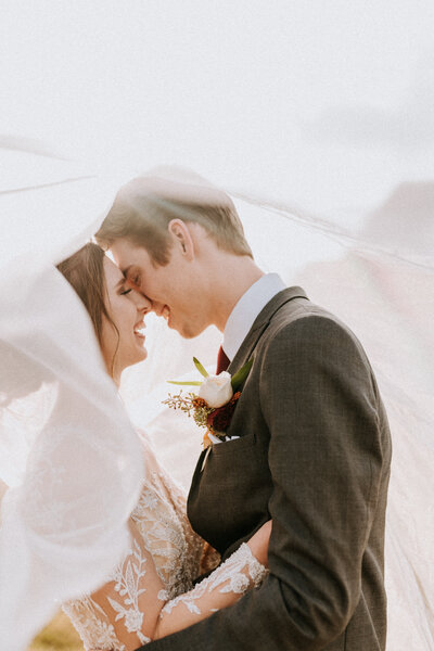 Bride and groom embrace with heads touching underneath veil