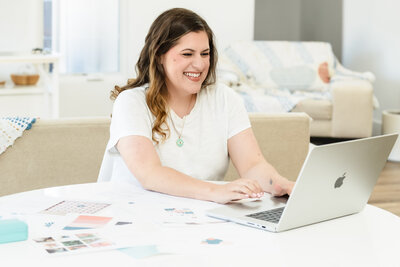 brand photo of a web designer working on her laptop, on a desk full of paper representing website ideas