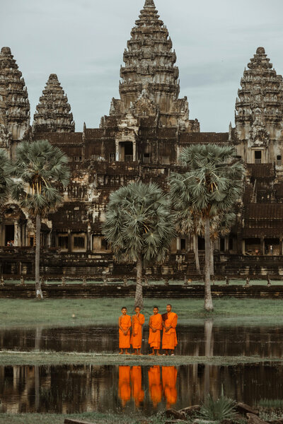 Group of Buddhist monks in orange robes standing by the reflecting pool at Angkor Wat, Cambodia.