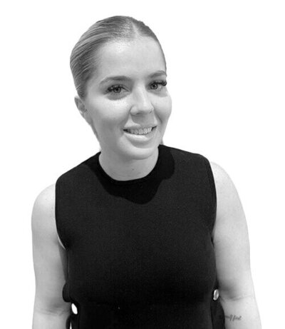 Junior Stylist with shoulder-length wavy hair and a sleeveless black top, showcasing a friendly and professional demeanour.