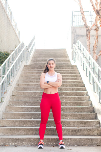 Sagan fitness is wearing red leggins and a white crop top. she is in front of city grey stairways.