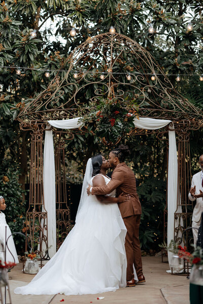 A bride and groom share their first kiss under a steel archway decorated in florals at the River Road and Jasmine House in Columbia, South Carolina.