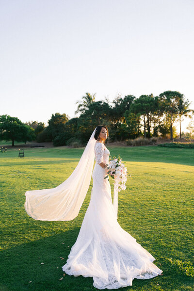 Bride holding bouquet with long flowing veil in a grassy field