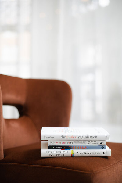 Stack of leadership and personal development books sitting on a brown velvet chair