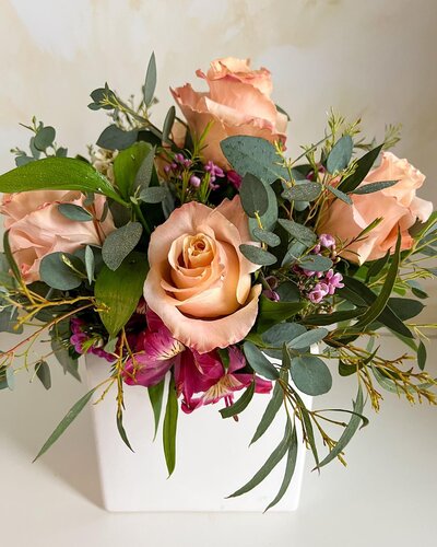 A close up of a floral arrangement with peach-colored roses and greenery.