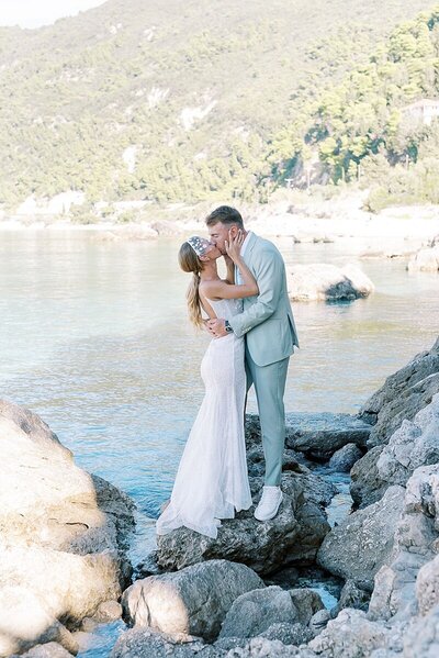 Bride and groom share a romantic kiss on the rocky coastline of Lefkada during their intimate destination wedding