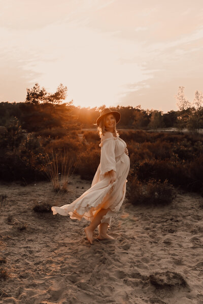 Zwangere vrouw in jurk poseert voor zwangerschapsshoot tijdens zonsondergang op de Kalmthoutse Heide