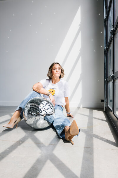 Woman sitting on floor with disco ball, with shadows from a large window on her face